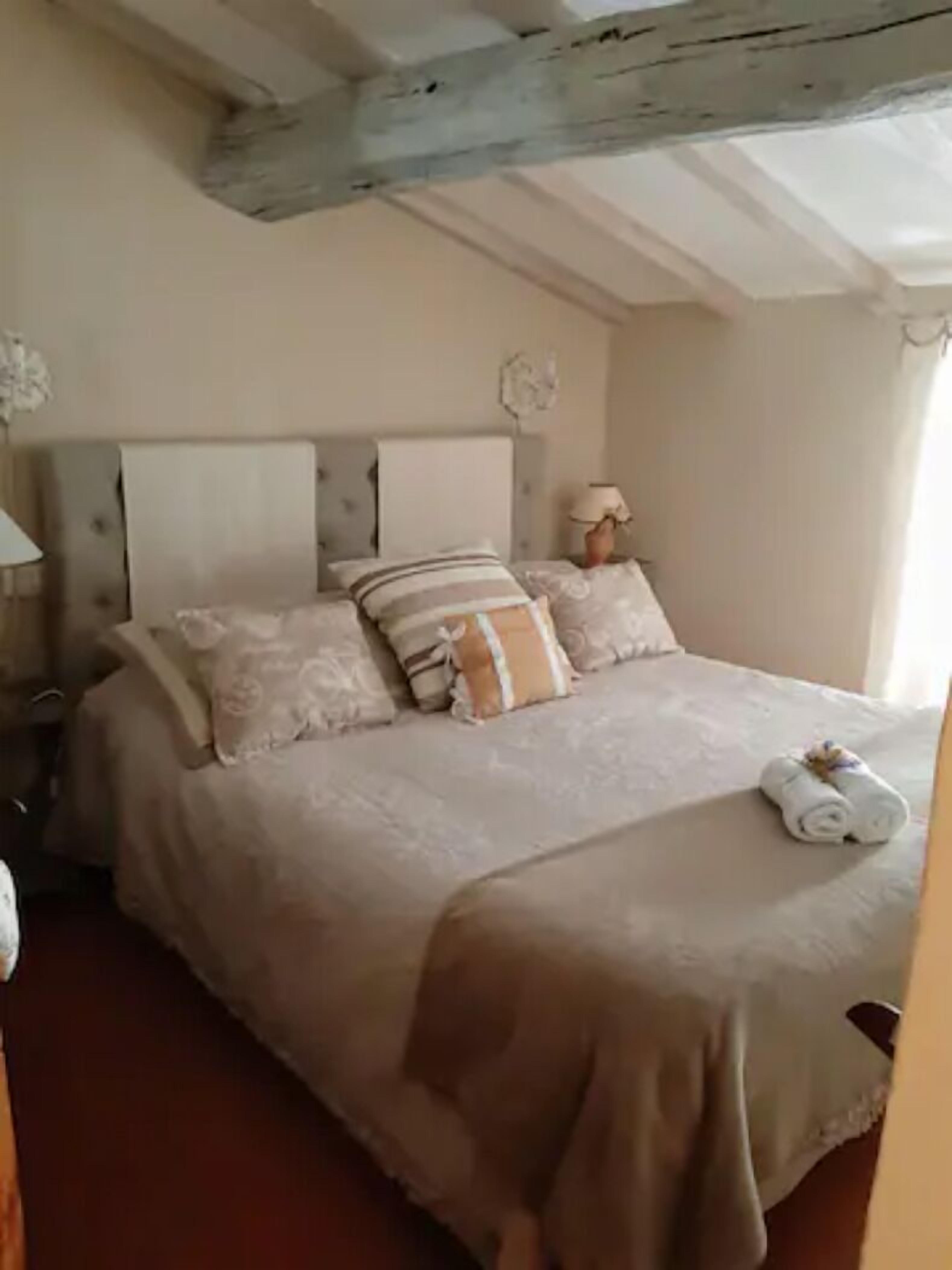 Una cama bien hecha con un cojín a rayas, una lámpara de noche y una toalla enrollada sobre la cama.