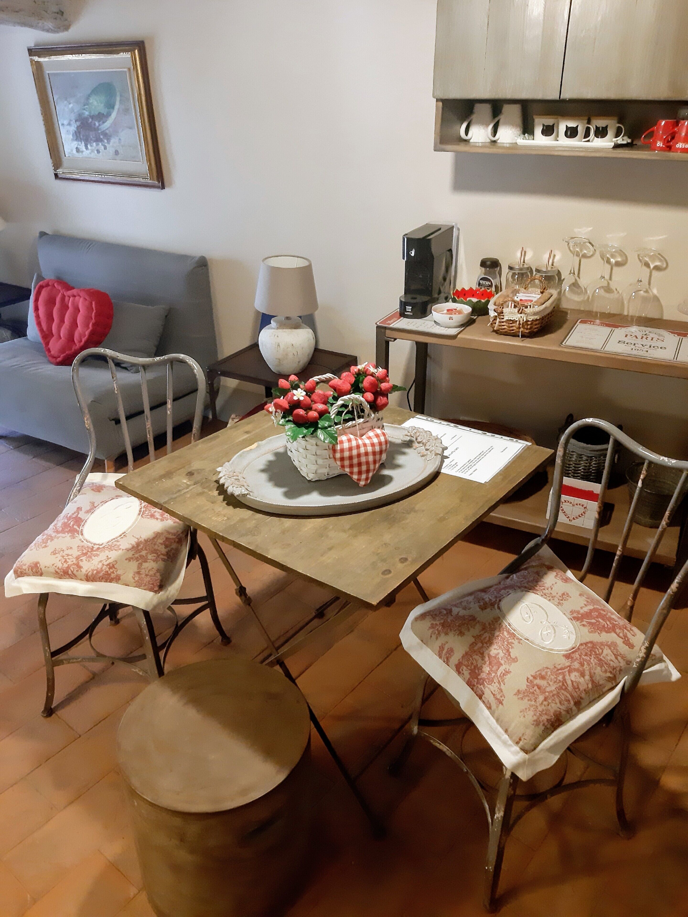 Un comedor con una mesa de madera, cuatro sillas, una cesta de fresas y una cafetera.