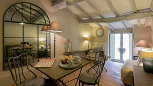 A dining area with a wooden table, chairs, and a mirror. There is a clock on the wall and a window with a view. - Cortona Shabby Chic House<br>(Independent & balcony) (Cortona)