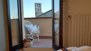A room with a view of a balcony, a white chair, a flower vase, and a towel with flowers. - Cortonas Rooftop Nest (Cortona)