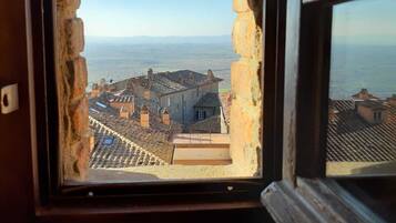 A window with a view of a coastal town, featuring terraced rooftops and a distant sea.