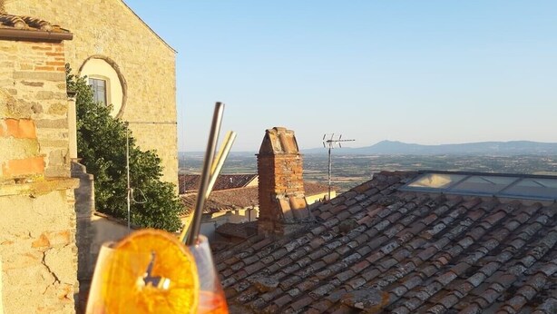 A balcony with a clear view of a distant landscape, a stone building, and a glass of orange juice. - Cortonas Rooftop Nest (Cortona)