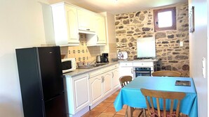Une cuisine compacte avec un réfrigérateur noir, des armoires blanches, un mur en pierre, une petite fenêtre et une table avec des chaises.