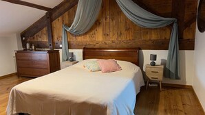 Une chambre avec un plafond en bois, un lit recouvert d’une courtepointe blanche, une table de chevet avec une lampe et une commode.