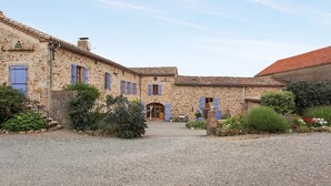 Un bâtiment en pierre avec une cour en gravier, une porte en bois et des volets bleus.