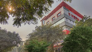 A modern building with a red and grey facade, large windows, and a sign indicating it is a hotel. - Treebo TMS Residency (New Delhi)
