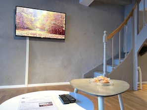 A room with a television displaying a nature scene, a small table with pastries, and a remote control on a white table. - Splendide Maison 5 chambres ! Quartier Historique (Limoges)