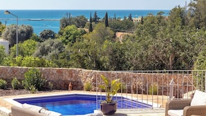 Un espace piscine aménagé avec des meubles en osier, un mur en pierre et une vue sur la mer.