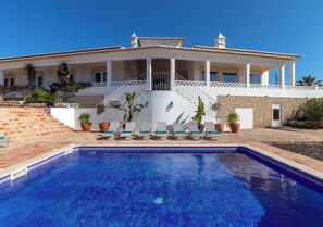 A large house with a swimming pool, a covered patio, and a stone wall.