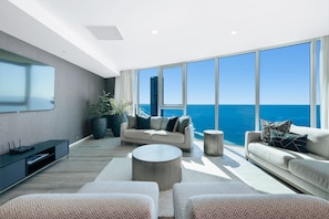 Una sala de estar moderna con un ventanal grande con vistas al océano, un sofá, una mesita de centro y un televisor sobre un mueble.