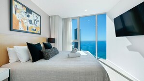 A modern hotel room with a large bed, a flat-screen TV, a painting on the wall, and a view of the ocean.