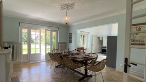 A spacious dining area with a large table and chairs, a chandelier, and a view of the outdoors through large doors. - A quaint vineyard gîte at Château Magdeleine Bouhou (Cars)