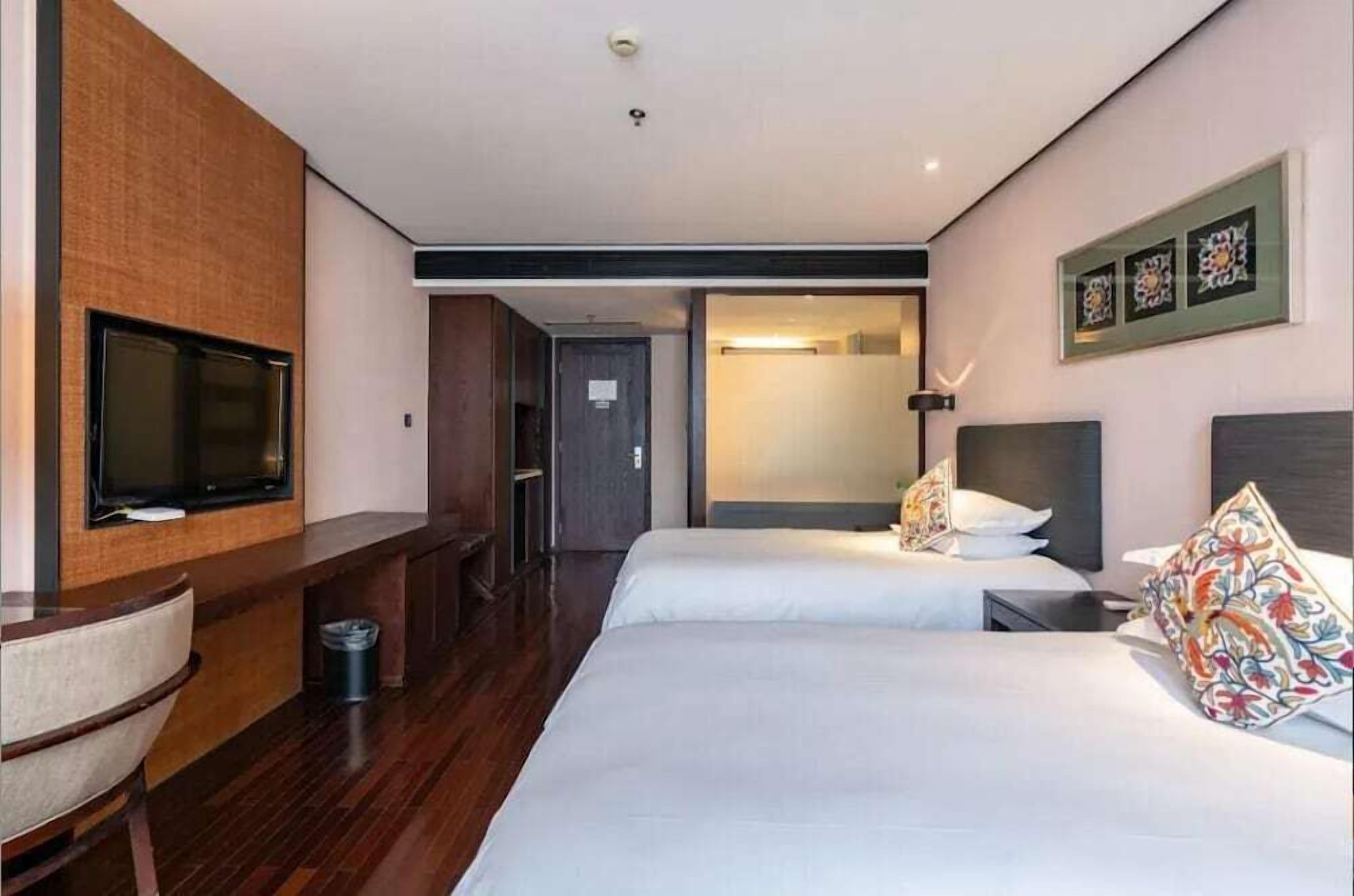 A hotel room with two beds, a TV, a desk, and a door leading to a bathroom.