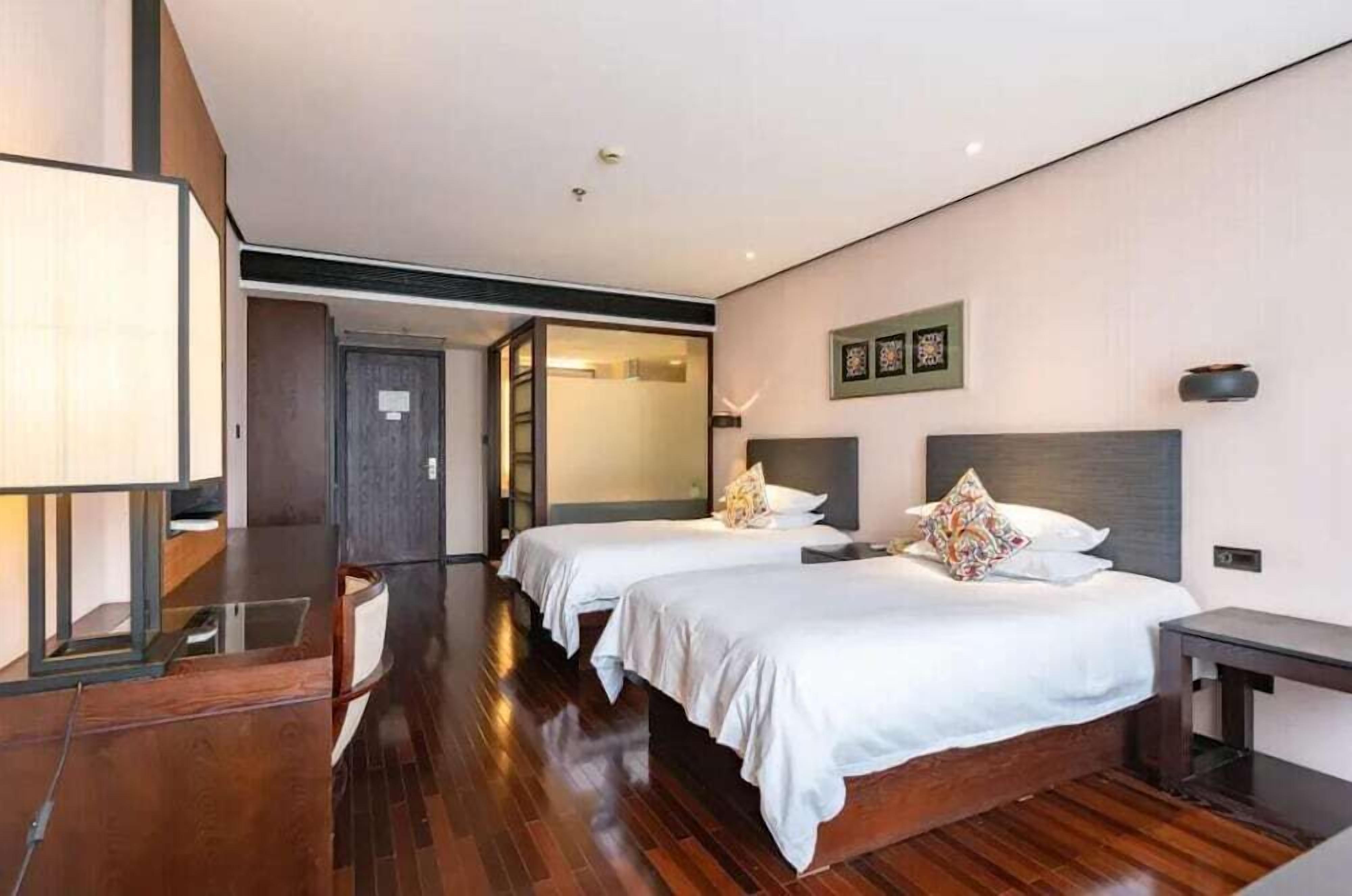 Habitación de hotel con dos camas, un escritorio, una silla y un ventanal grande.