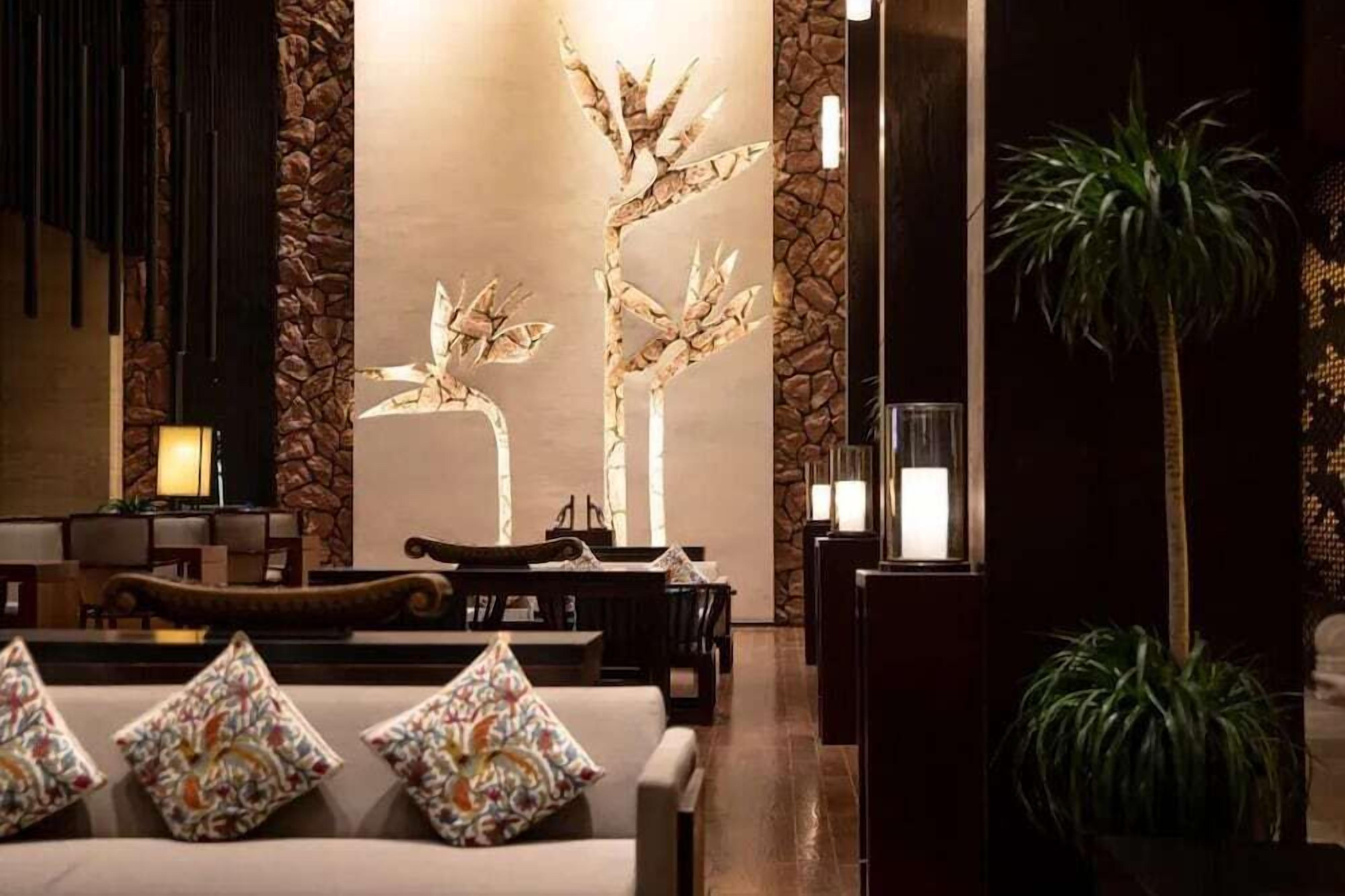 A lobby with a stone wall, a reception desk, a sofa with patterned cushions, and a tall plant.
