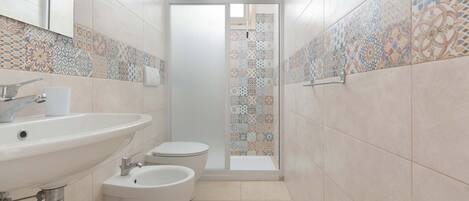 A modern bathroom with a large sink, toilet, bidet, and a shower area.