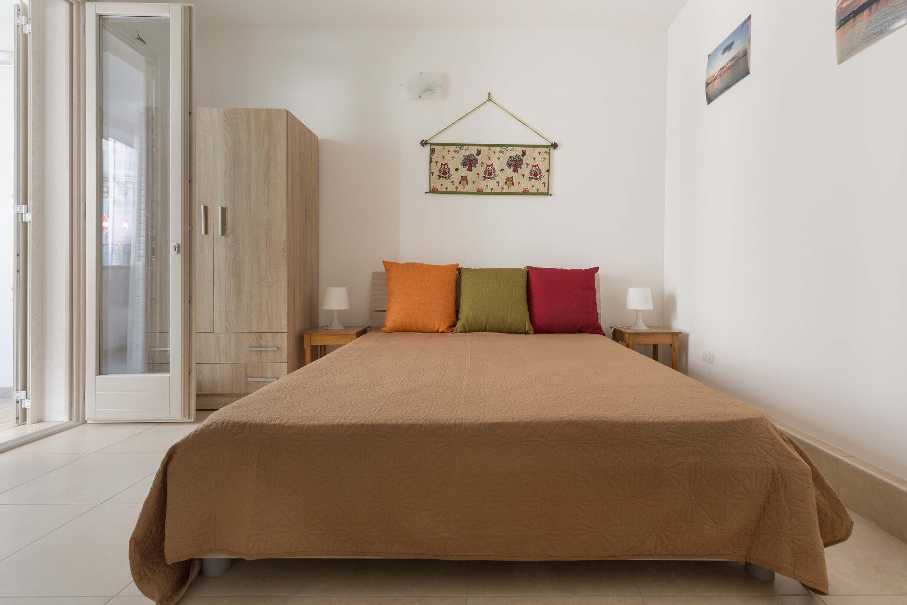 A bedroom with a large bed, a wardrobe, a bedside table with a lamp, and a wall-mounted picture.