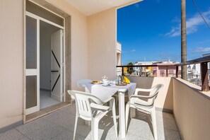 A balcony with a table set for two, chairs, and a view of buildings in the background. - Carlotta`s House by BarbarHouse (San Foca)