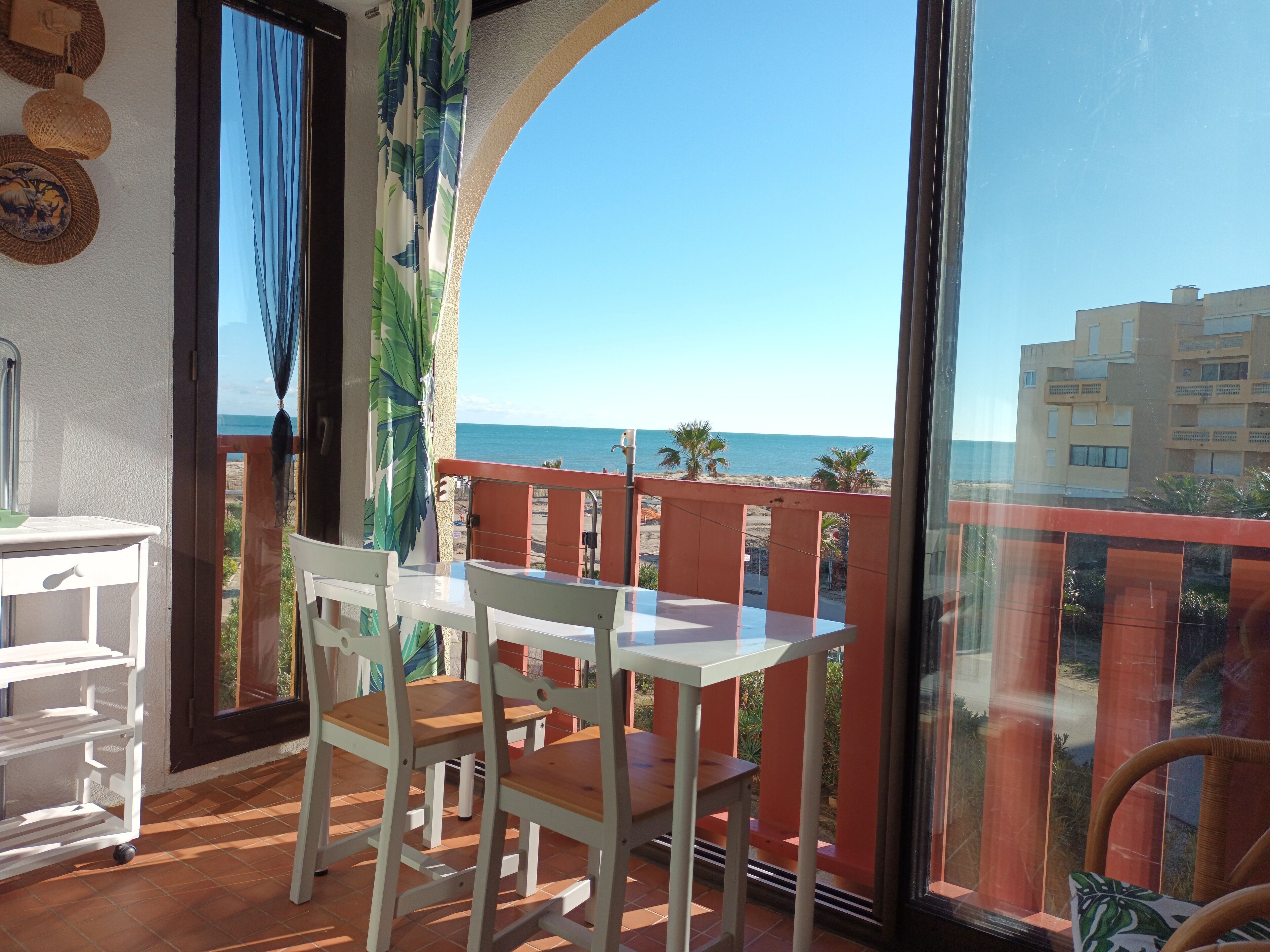 A balcony with a table and chairs, a view of the sea, and a building in the background.