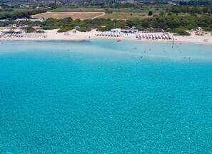 An aerial view of a beach with clear turquoise waters, a sandy shore, and several beach umbrellas and sun loungers. - Appartamento Sara by BarbarHouse (Gallipoli)