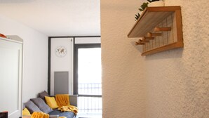Une pièce avec un lit, une fenêtre, une porte et une étagère fixée au mur, sur laquelle se trouve une plante.