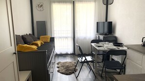 Un espace de vie compact comprenant un lit, une table à manger, des chaises, un téléviseur et un petit coin cuisine.