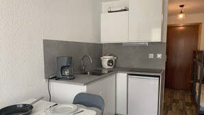 Une cuisine compacte équipée d’une machine à café, d’un évier, d’un lave-vaisselle et d’un coin repas avec une table dressée pour deux personnes.