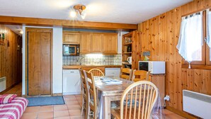 Eine kompakte Küche mit Holzausstattung, einem Esstisch mit Stühlen, einer Mikrowelle und einem kleinen Kühlschrank.