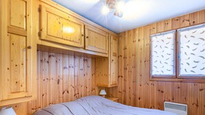 Ein Zimmer mit Holzwandverkleidung, einem Bett, einem Nachttisch, einer Lampe und einem Fenster mit Feder-Motiv.