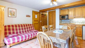 Ein gemütlicher Wohnbereich mit einem karierten Sofa, einem Holzesstisch, Stühlen und einer Küche mit Holzschränken und einer Mikrowelle.
