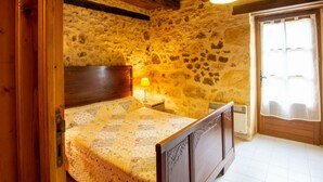 Een eenvoudige slaapkamer met stenen muren, een houten bed, een klein nachtkastje en een hanglamp.
