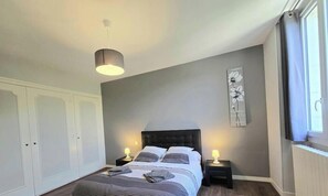 A bedroom with a bed, bedside tables, a wardrobe, a wall clock, and a window. - Charming stone house in Coly (Coly-Saint-Amand)