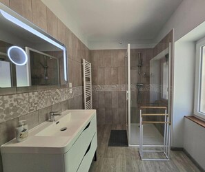 A modern bathroom with a large mirror, a shower, and a vanity with a sink.