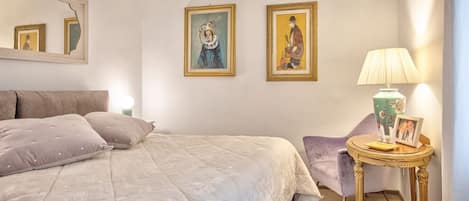 A bedroom with a bed, a chair, a lamp, and two framed pictures on the wall.