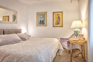 Ein Schlafzimmer mit einem Bett, einem Sessel, einer Lampe und zwei gerahmten Bildern an der Wand.