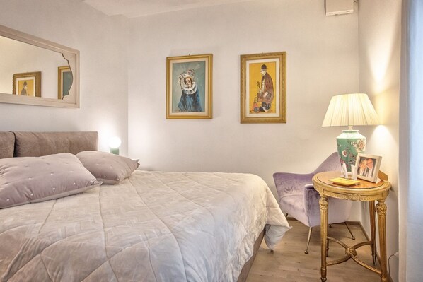 A bedroom with a bed, a chair, a lamp, and two framed pictures on the wall.