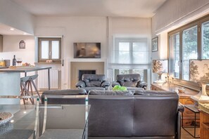 A modern living room with a glass coffee table, leather sofas, a fireplace, and a kitchen area with a bar.