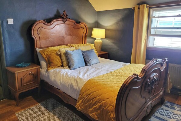 A bedroom with a wooden bed, a bedside table, a lamp, and a window with curtains. - The Little Townhouse - Southwell (Southwell)