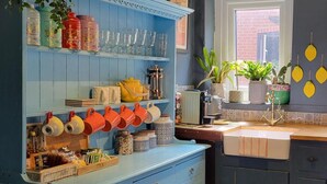 A kitchen with blue cabinets, a sink, and various kitchen items like mugs and jars. - The Little Townhouse - Southwell (Southwell)