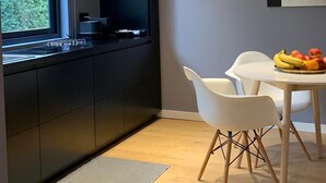 A modern kitchen with a built-in stove, a dining area with a white table and chairs, and a large window providing a view of greenery outside. - LeMummarelle36Apartment (Naples)