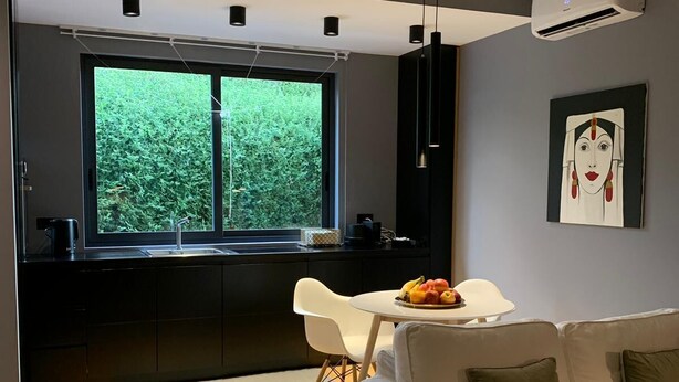 A modern kitchen with dark cabinetry, a large window, and a dining area with a white table and chairs. - LeMummarelle36Apartment (Naples)