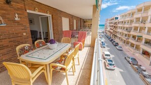 A balcony with a table and chairs, a view of the street, and a building with balconies. - Fidalsa Bay View Romance (Guardamar)