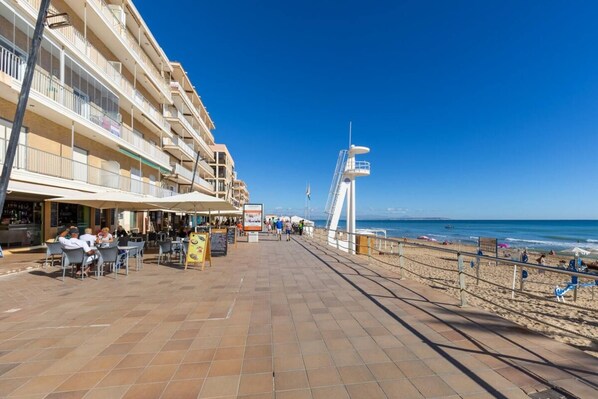 A beachfront promenade with outdoor seating, a lifeguard tower, and a view of the sea.