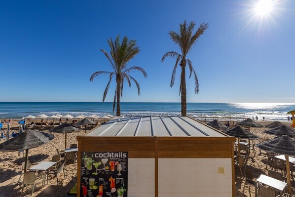 A beachside bar with a menu board, palm trees, and beach umbrellas.