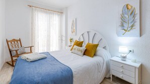 A bedroom with a bed, a chair, a bedside table with a lamp, and a wall-mounted artwork. - Fidalsa Bay View Romance (Guardamar)