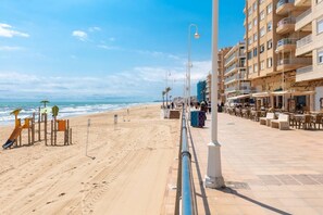 A beachside promenade with a sandy beach, a playground, and a row of outdoor seating areas. - Fidalsa Bay View Romance (Guardamar)