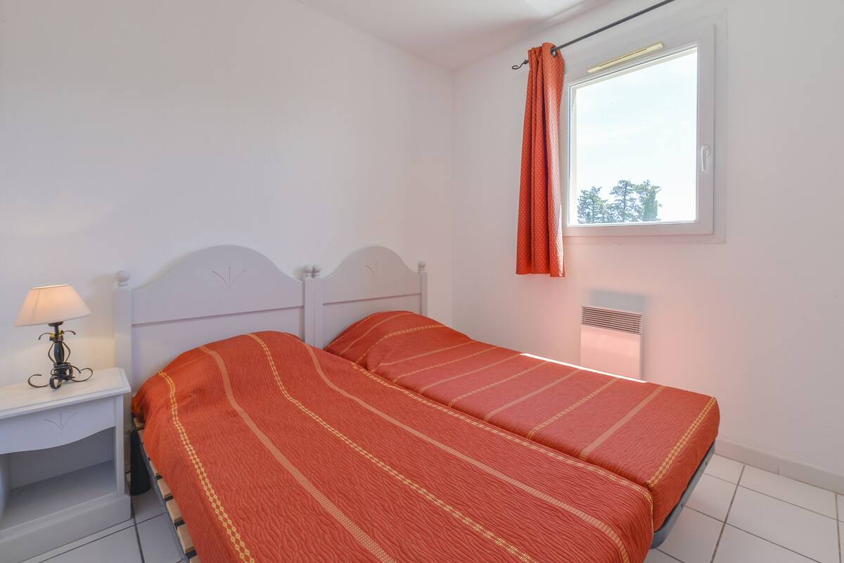 Een slaapkamer met een bed, nachtkastje, lamp, raam met gordijnen en een radiator.