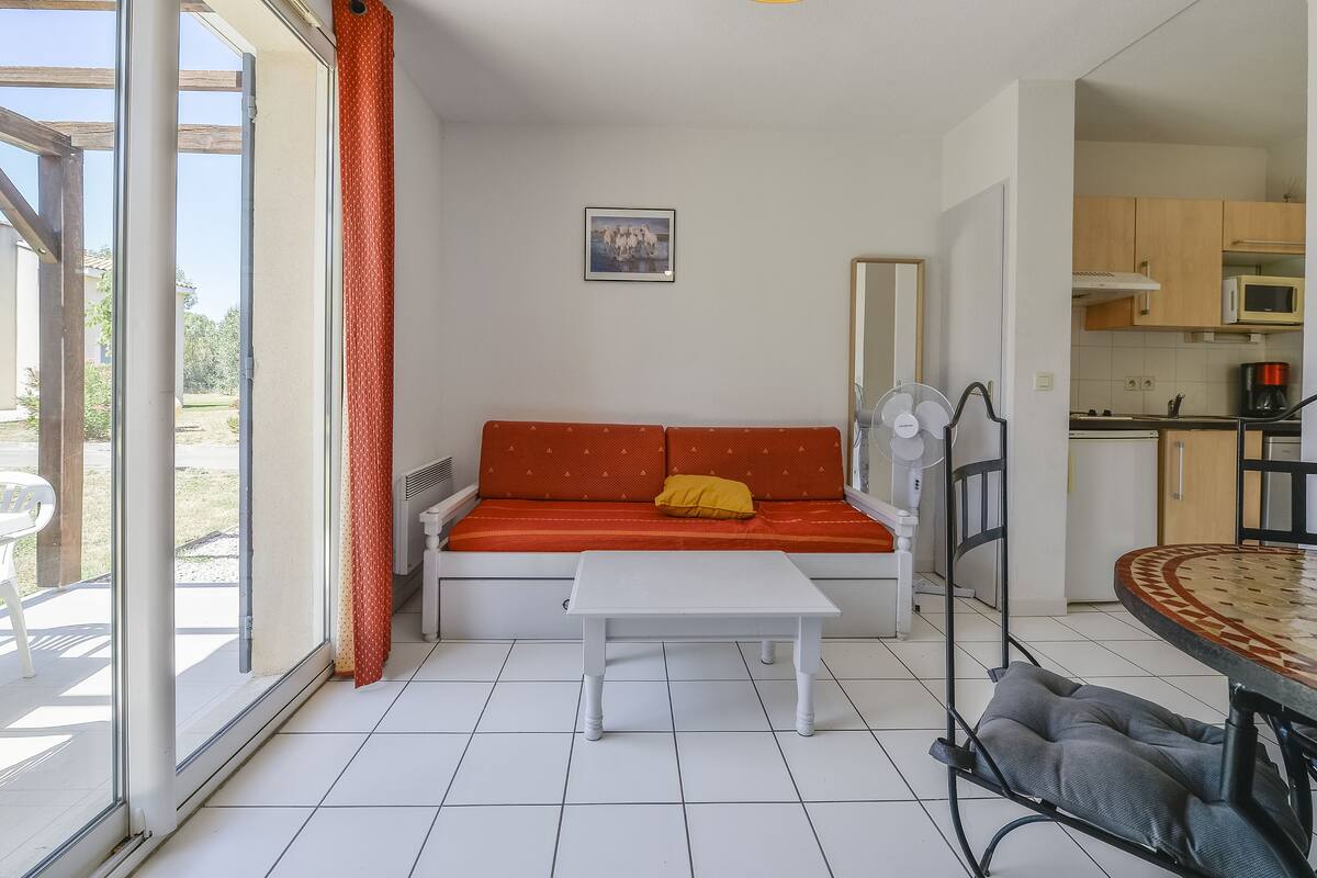 Een kamer met een bank, een tafel, een ventilator en uitzicht door een groot raam.