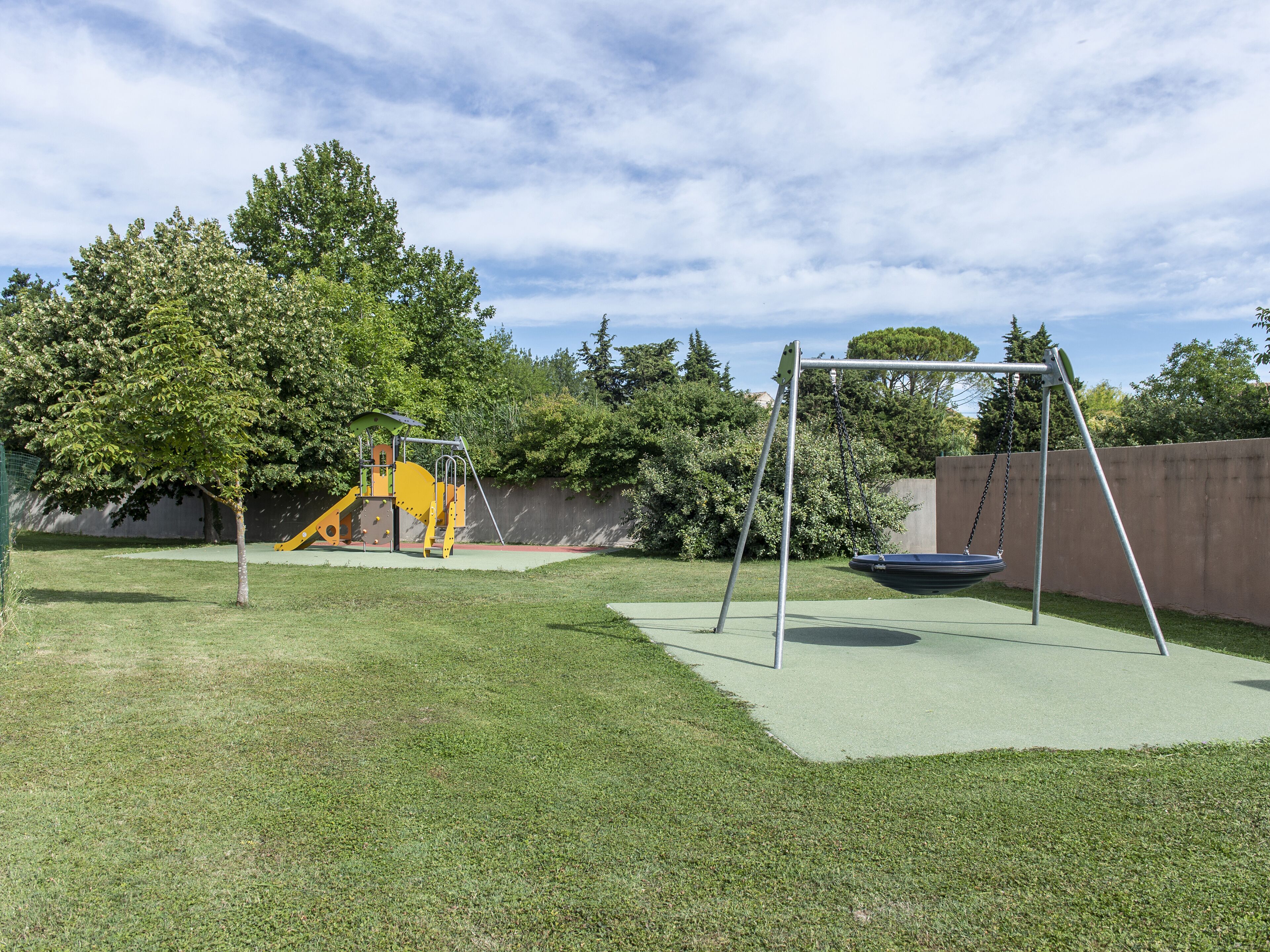 A playground with a swing set and a slide, surrounded by grass and trees.