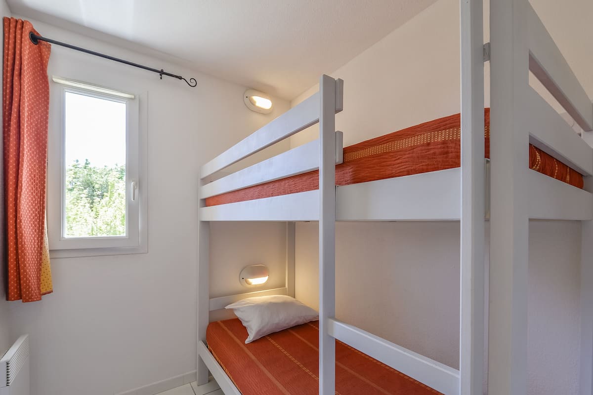 Een slaapkamer met een stapelbed, raam, gordijnen en een radiator.